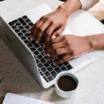 person using Macbook pro beside white ceramic mug