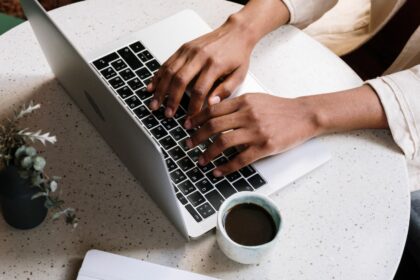 person using Macbook pro beside white ceramic mug