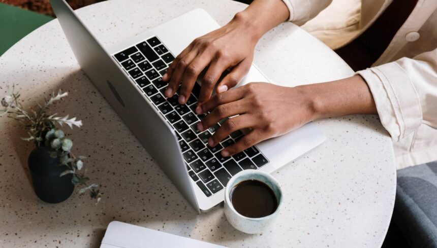 person using Macbook pro beside white ceramic mug